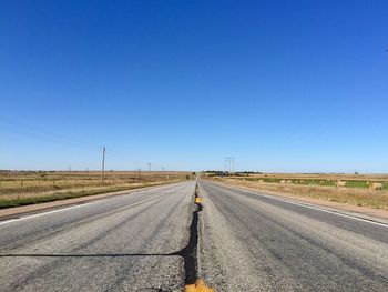 Empty road leading towards clear blue sky