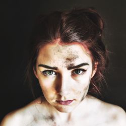 Close-up portrait of young woman with dirty face against black background