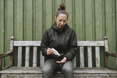 Woman on bench applying antibacterial gel on her hands