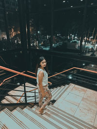 Full length portrait of young woman moving down on steps at night