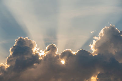 Low angle view of sunlight streaming through clouds