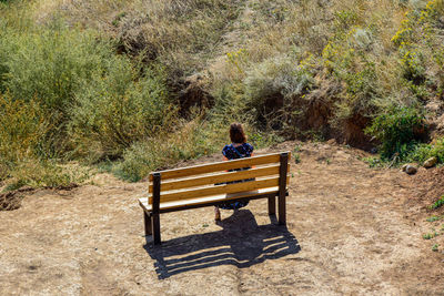 Rear view of woman sitting on bench in field