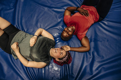 Directly above shot of happy female athletes lying on safety mat at sports court