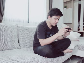 Young man using smart phone while relaxing on sofa at home