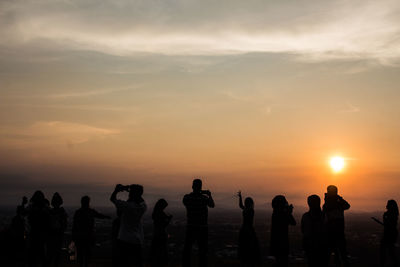 Silhouette people standing by sea against sky during sunset