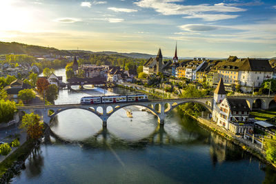 Bridge over river by buildings against sky