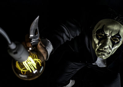 High angle view of man wearing mask holding illuminated light bulb against black background