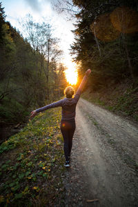 Rear view of woman standing on road in forest