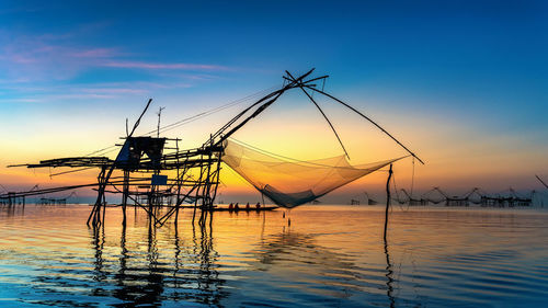 Silhouette fishing net by sea against sky during sunset