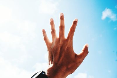 Cropped hand of man gesturing against blue sky