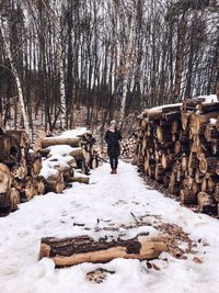 Woman standing amidst logs on snow covered field