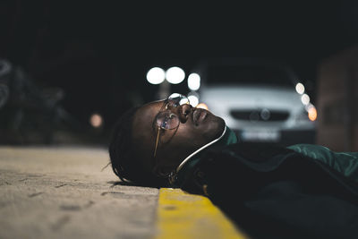 Close-up of thoughtful young man lying down on sidewalk at night