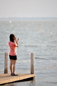 Rear view of woman standing on sea shore against sky