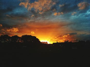 Silhouette trees against dramatic sky during sunset