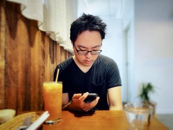 Asian man using mobile phone at table in cafe with copy space.
