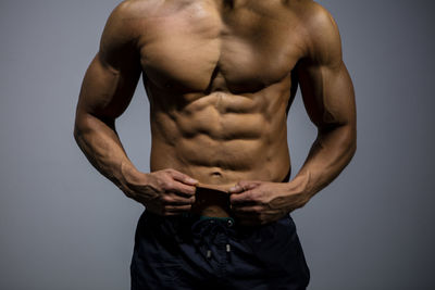 Midsection of muscular man standing against gray background