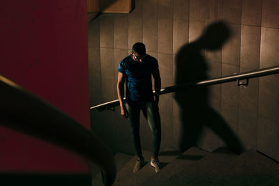 Concentrated young black athlete with sports clothing and sunglasses standing on the stairs before competition