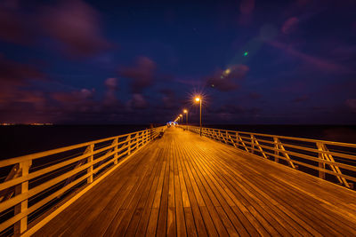 Illuminated bridge over sea against sky at night