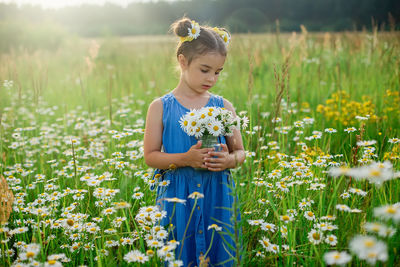 Cute little girl, holding a jar with a bouquet of daisies, in a field