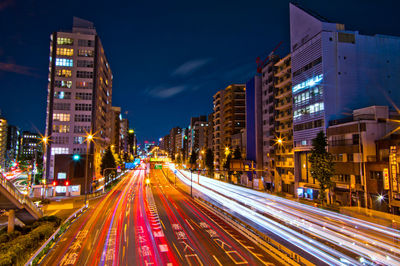 Light trails on city street amidst buildings at night