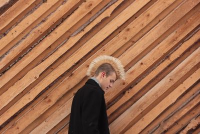 Side view of young man with hairstyle standing by wooden wall