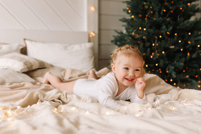 Happy cheerful baby little girl sitting smiling on a cozy bed at christmas holidays at home