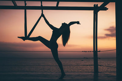 Silhouette woman with arms outstretched standing at beach against sky during sunset