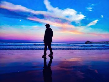 Silhouette man standing on beach against sky during sunset