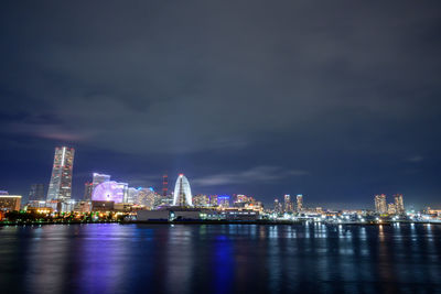 Illuminated city by river against sky at night