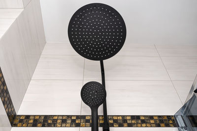 A modern, black metal shower with small and large rain shower, placed on tiles.