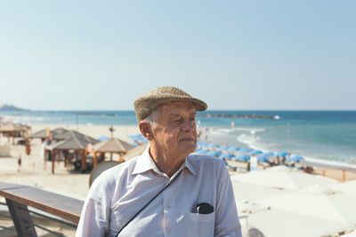 Senior man looking away while standing against beach