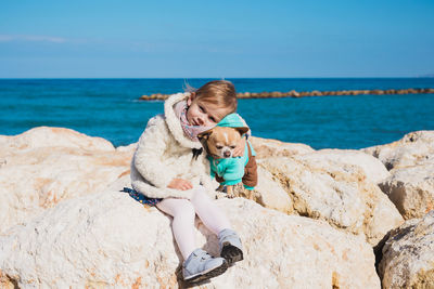 Portrait of cute girl with dog sitting on rock