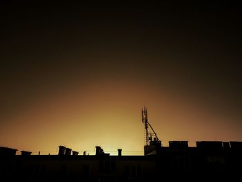 Silhouette cranes in city against clear sky