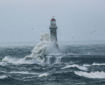 Lighthouse by sea against clear sky