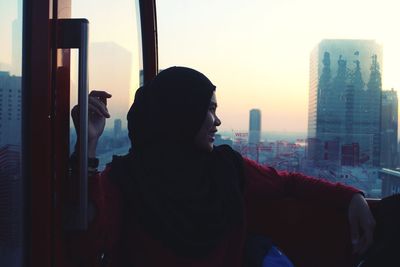 Young woman looking through window during sunset