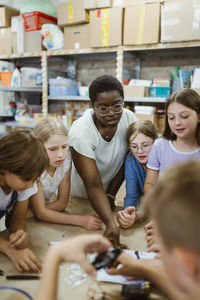 Female teacher assisting group of students working on robotics project at workshop