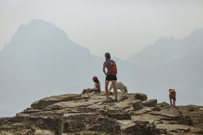 Female hikers with dogs on mountain against sky