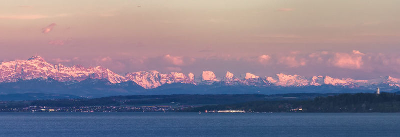 Scenic view of sea by mountains against sky during sunset