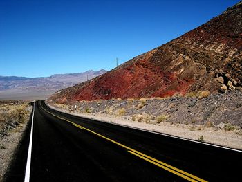 Road leading towards mountains against clear blue sky