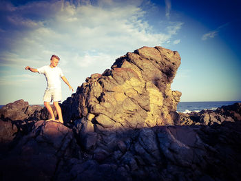 Teenage boy standing on rock formation by sea