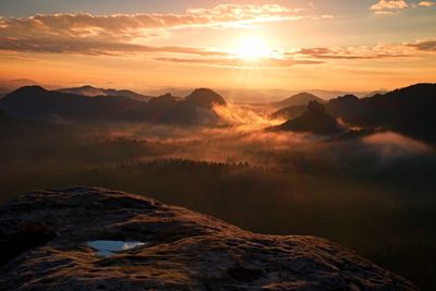 View over sandstone cliff into deep misty valley in saxony switzerland. peaks increased from fog