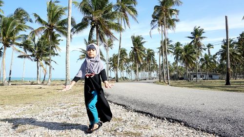 Girl walking at roadside against palm trees