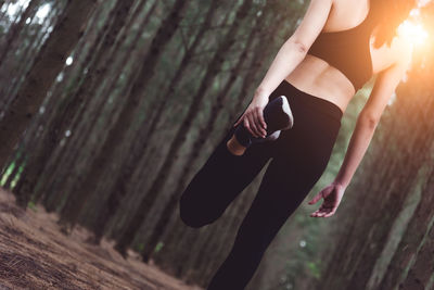 Low section of woman exercising against trees in forest