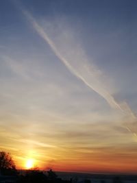 Low angle view of silhouette vapor trail against sky during sunset