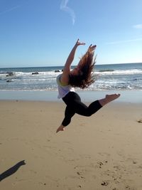 Woman jumping on beach against sky