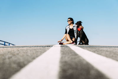Woman with dog and skateboard against clear blue sky