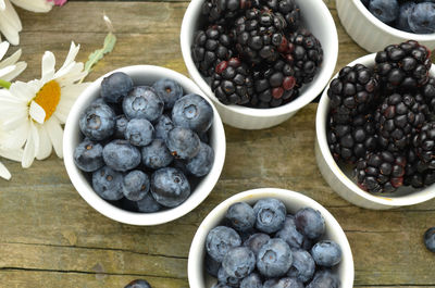 Blueberries and blackberries in small white ramekins with garden daisies on rustic wood table