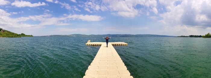 Mid distant view of woman standing on pier against sky