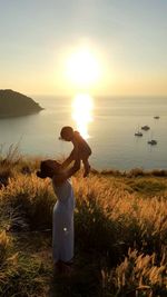 High angle view of mother carrying daughter while standing by sea during sunset