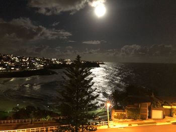 Illuminated buildings by sea against sky at night